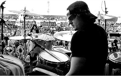 Black-and-white photo from behind Randy Lane's drum kit looking out at a large outdoor festival crowd