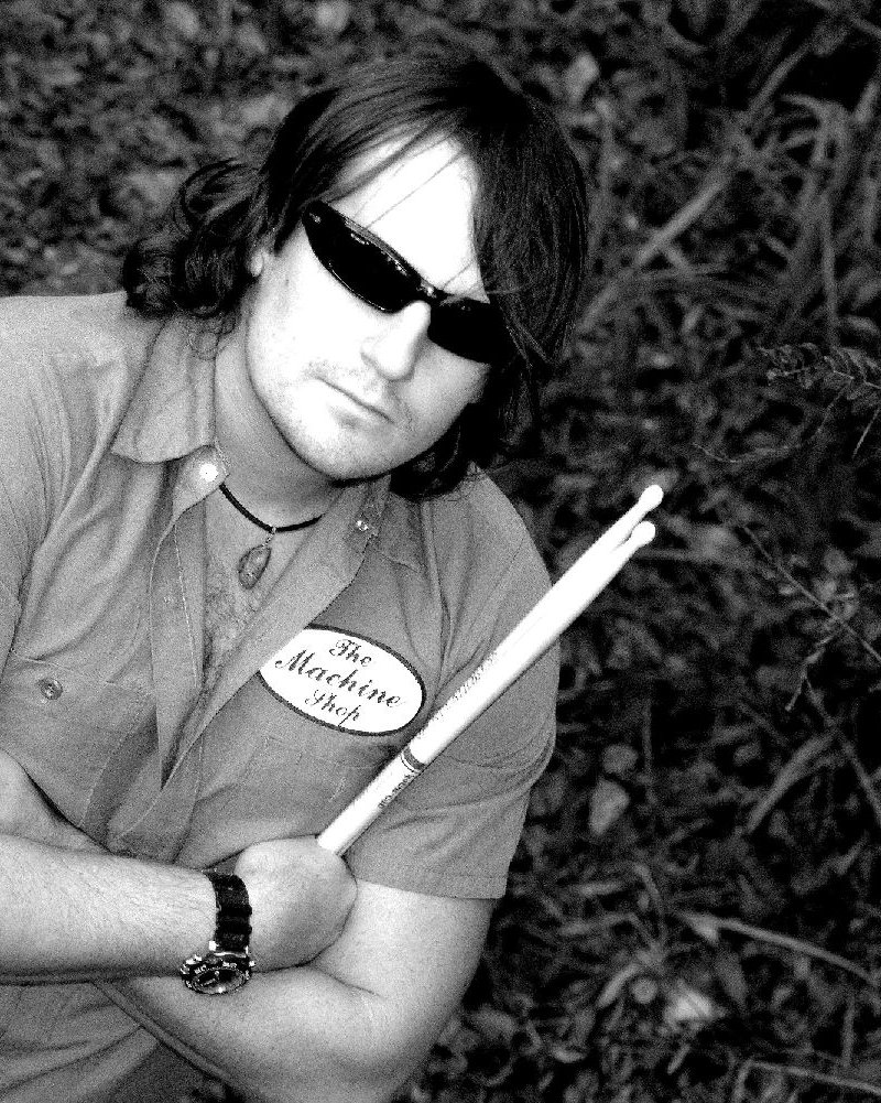 Black-and-white portrait of drummer Randy Lane in sunglasses, arms crossed, holding drumsticks